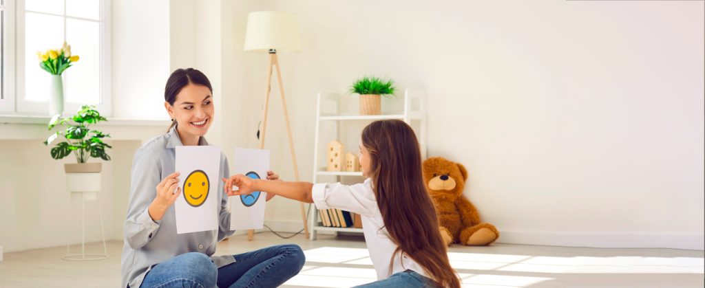 Autismo y ABA Principal: Terapeuta sosteniendo imágenes de dos expresiones faciales mientras el niño pinta la imagen de la cara feliz