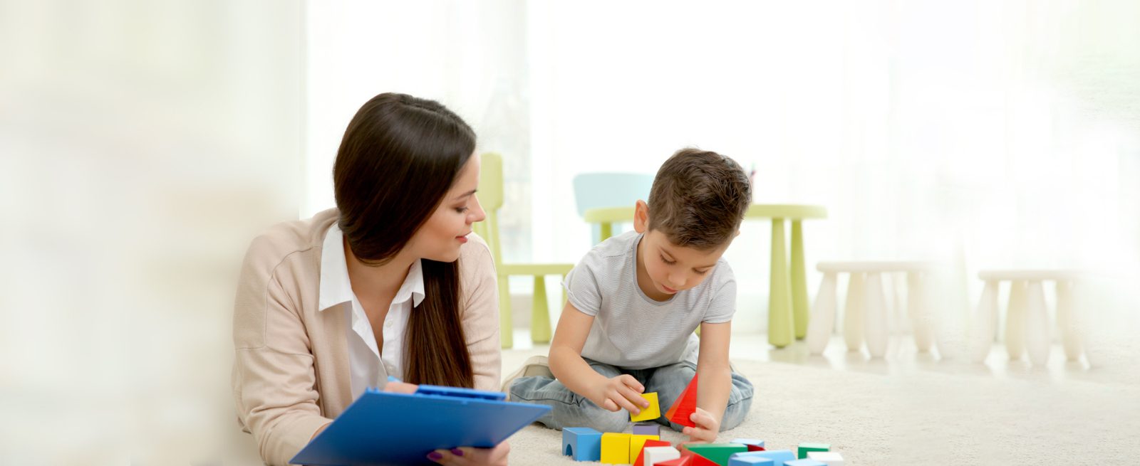 Autism & ABA: Children's Center for Autism: Therapist observes child playing with blocks on the floor
