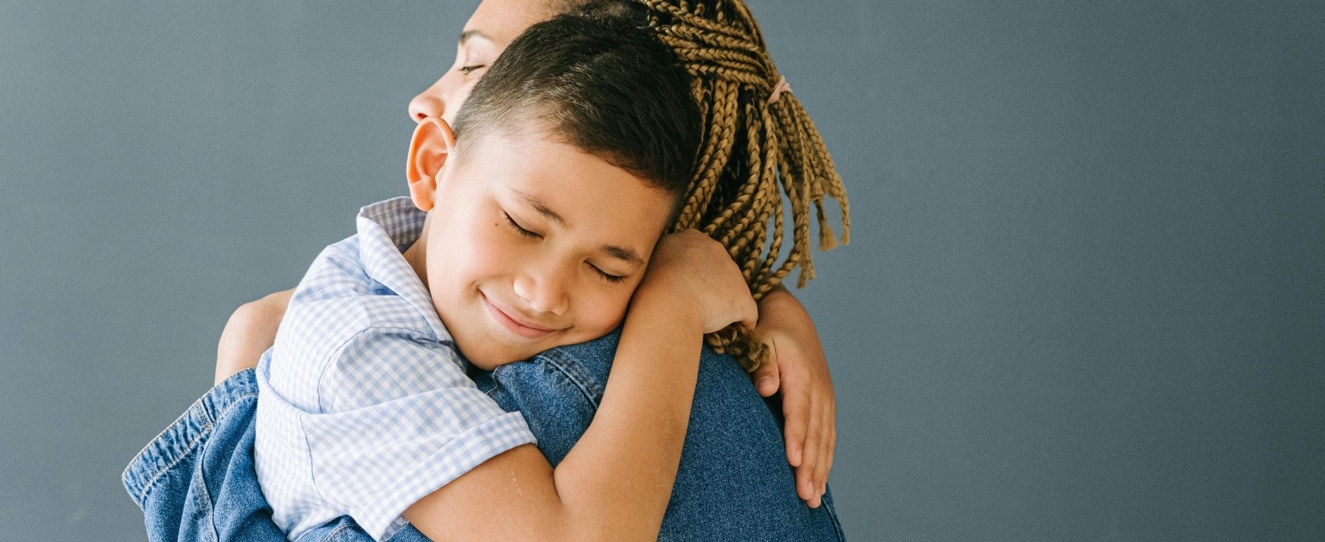 A young boy hugs a woman with a tight, restrained smile on his face.