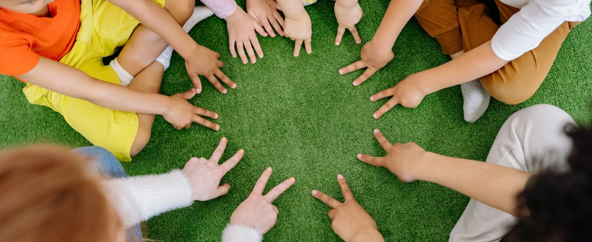 Children sit together in a circle, using their hands to play a game or activity.