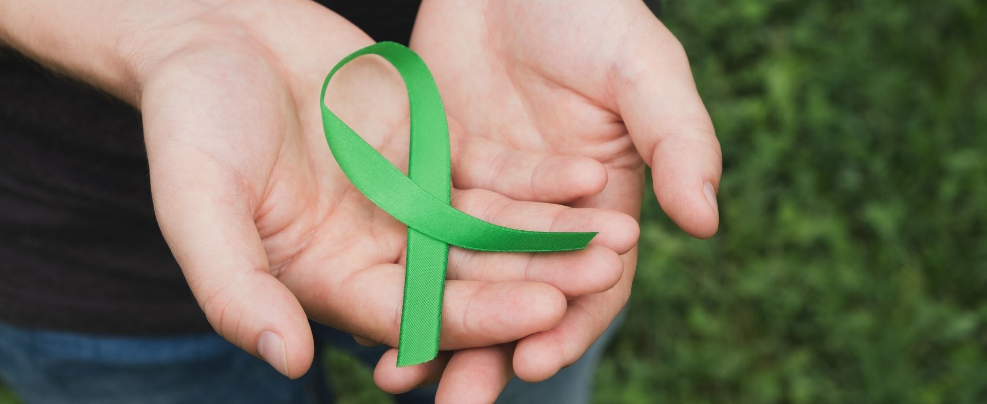 Hand holding a green awareness ribbon